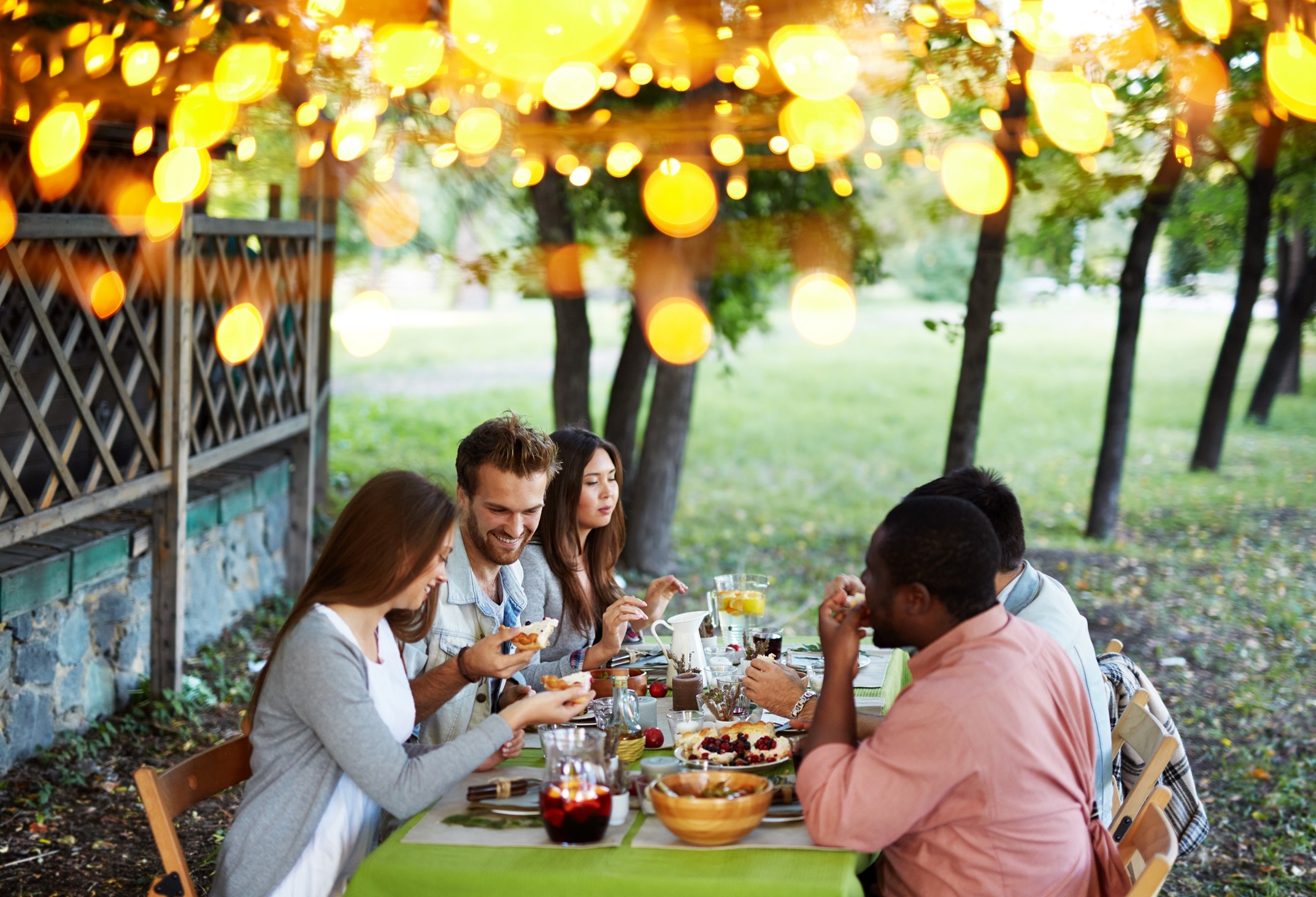 A diverse group of young adults seated around an outdoor table laden with traditional thanksgiving foods on a beautiful fall day 