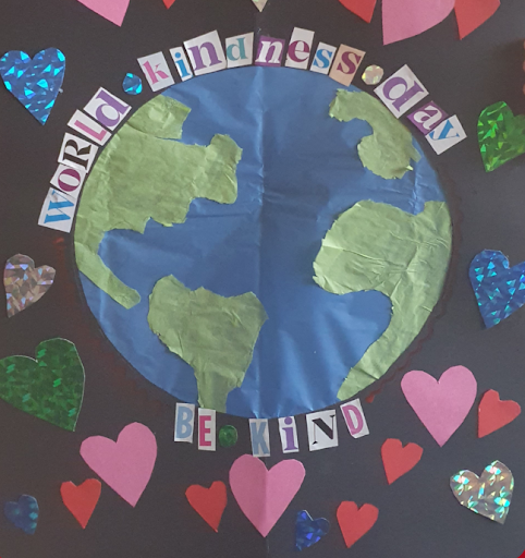 Image of a classroom bulletin board decorated with construction paper for World Kindness Day. Black background with a globe and construction paper hearts taped to the black background. Letters cut out of a magazine that spell out world kindness day. be kind. 