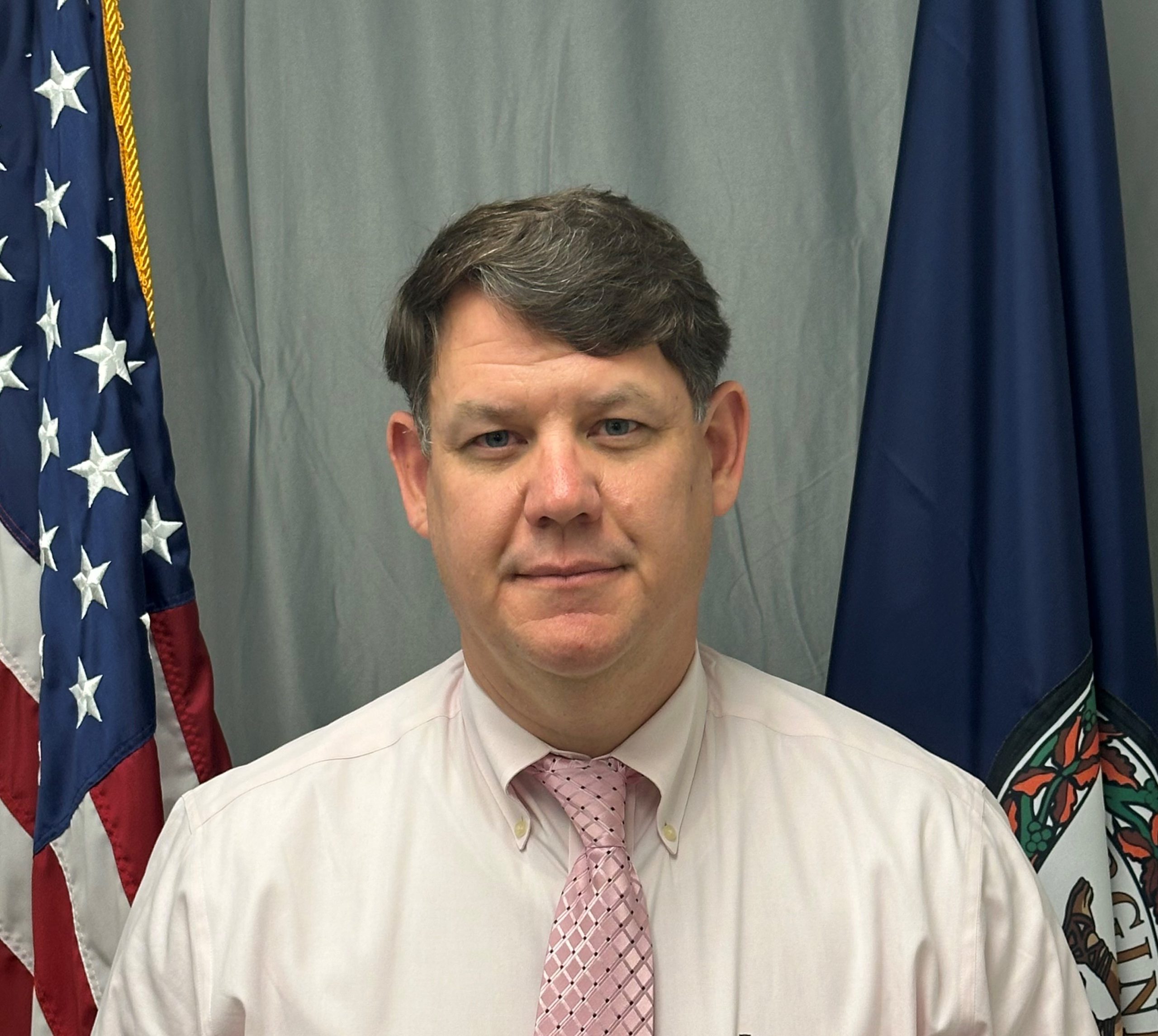 Detective Sergeant Steve Brunelle stands with a grey curtain and both the American and Virginia flags behind him.