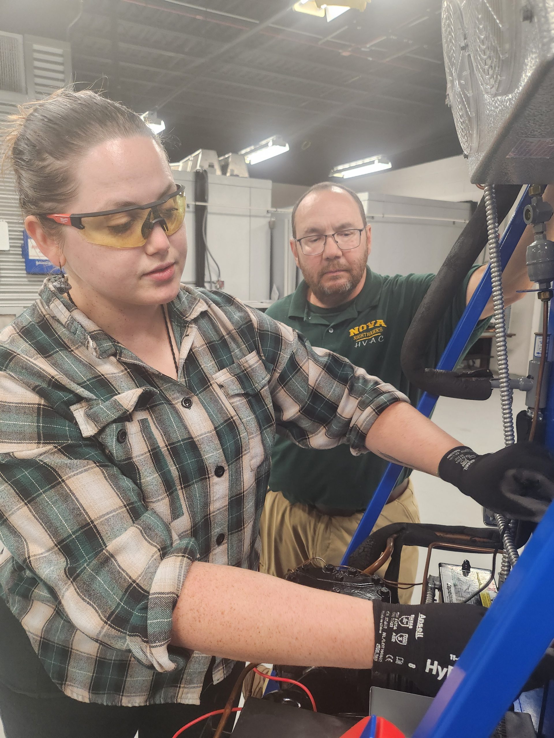Program Head John Meeker watches a young woman who is an AIR student work on a piece of equipment.