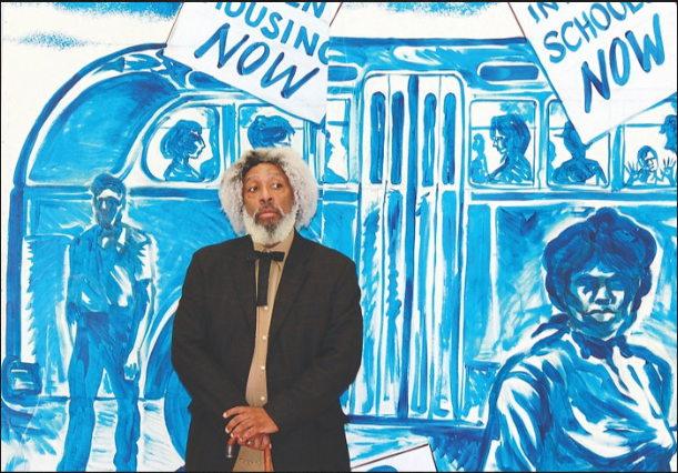 Nate Richardson stands before a mural made with only blue paint on a white background, depicting an old city bus with African American riders. "Frederick Douglass juxtaposed with civil rights images in the background. Hampton Center for the Performing Arts"