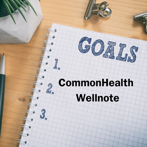 A spiral notebook with graph paper rests on a wooden desk with a plant, pencil and binder clip. The first page of the notebook says GOALS with numbering 1. 2. 3. and black text that says CommonHealth Wellnote