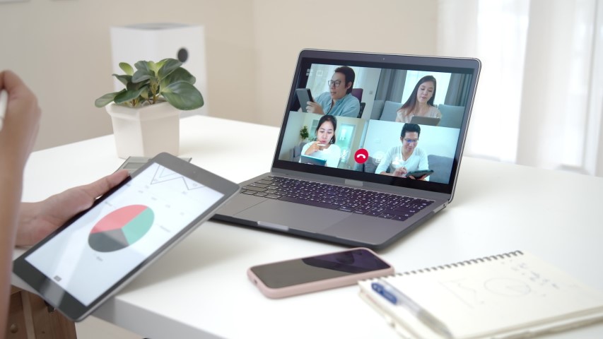 Photo of a laptop with four students on the screen, and a person in the foreground with a tablet with a pie chart in red, green and black.