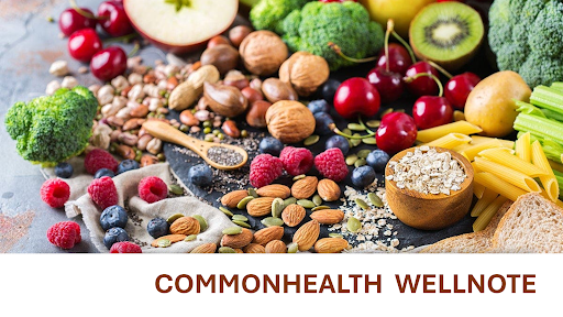 A colorful assortment of healthy foods is displayed on a textured surface. The spread includes fresh fruits such as apples, cherries, raspberries, and blueberries, along with green vegetables like broccoli and celery. Nuts, seeds, and whole grains, including almonds, walnuts, oats, and pasta, are also present. A wooden spoon filled with chia seeds is placed among the ingredients. The text "COMMONHEALTH WELLNOTE" is written in bold, brown letters at the bottom of the image.