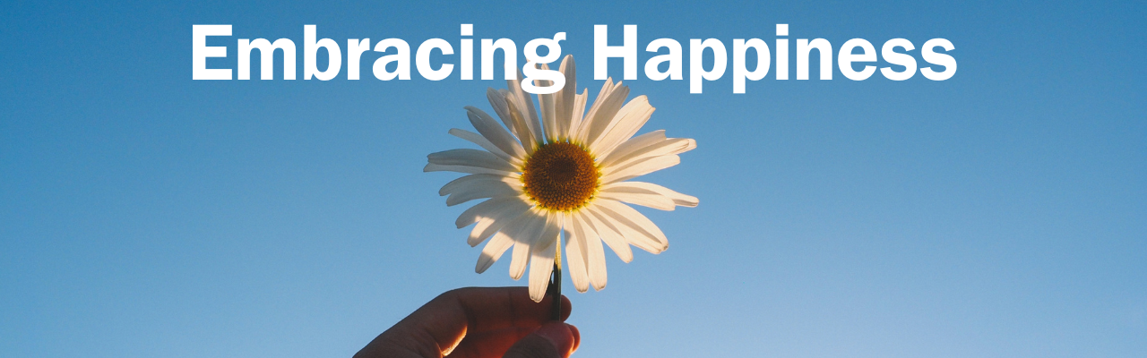 Stock photo of a hand holding up a white gerbera daisy against a cloudless blue sky. "Embracing Happiness" appears in white text at the top of the image. 